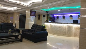 A lobby with a reception desk, two leather sofas, a coffee table, and a chandelier. - Le Privilege Hotel (Oran)