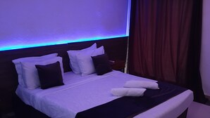 Una cama bien hecha, con almohadas blancas y oscuras, cabecero oscuro y una tira de luz ambiental azul.