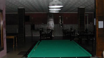 Una mesa de billar en una habitación con poca luz, con azulejos estampados en el techo y una lámpara colgante.