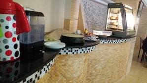 A kitchen area with a coffee machine, a polka-dotted mug, a cake stand, and a chocolate display. - Le Privilege Hotel (Oran)