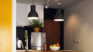 Una cocina moderna con un refrigerador de acero inoxidable, una encimera de madera, dos taburetes de bar, lámparas colgantes y una planta en maceta.
