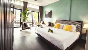 Habitación de hotel con una cama grande, zona de estar con una silla y mesa, una planta en maceta y vistas por la ventana.