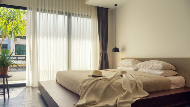 Un dormitorio moderno con una cama grande, una mesita de noche, una planta en maceta y vistas a la calle.