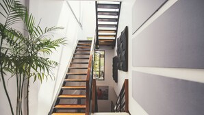 Una escalera con escalones de madera y barandas de metal, una planta en maceta y un cuadro colgado en la pared.