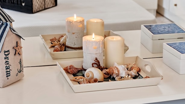 Un dormitorio ordenado con cama, mesitas de noche y cómoda. Hay velas sobre las mesitas y una caja decorativa con conchas marinas.