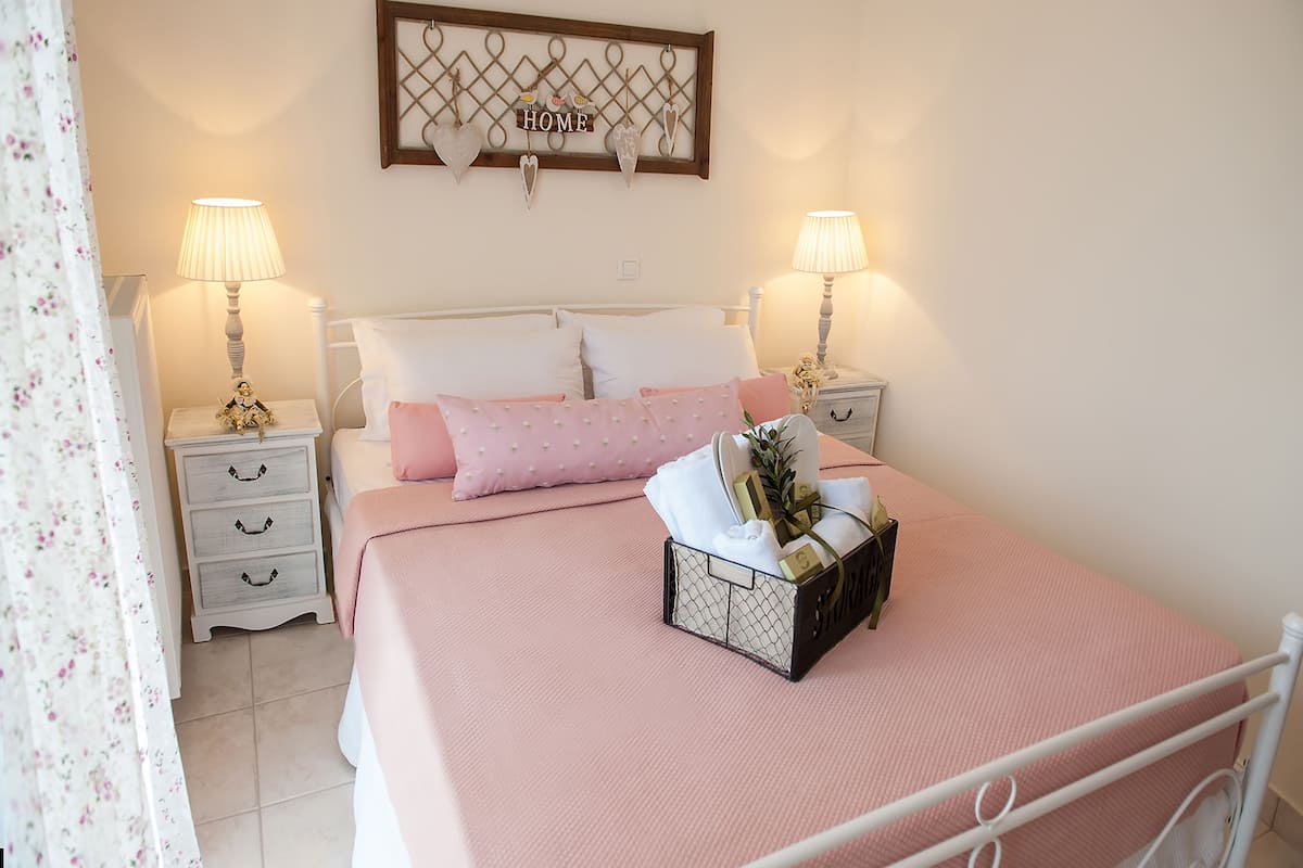 A neatly arranged bedroom with a bed, two bedside tables, a nightstand, a decorative wall hanging, and a floral curtain.