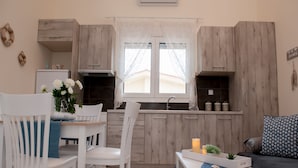 Una cocina moderna con armarios de madera, un comedor con sillas blancas, una mesa pequeña con mantel azul y un sofá con cojines estampados.