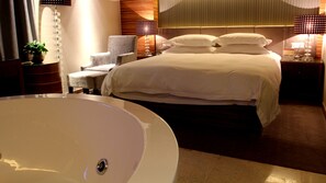 A hotel room with a large white bathtub, a bed with white linens, a chair, and two bedside lamps. - Yiwu Wendemu International Hotel (Jinhua)