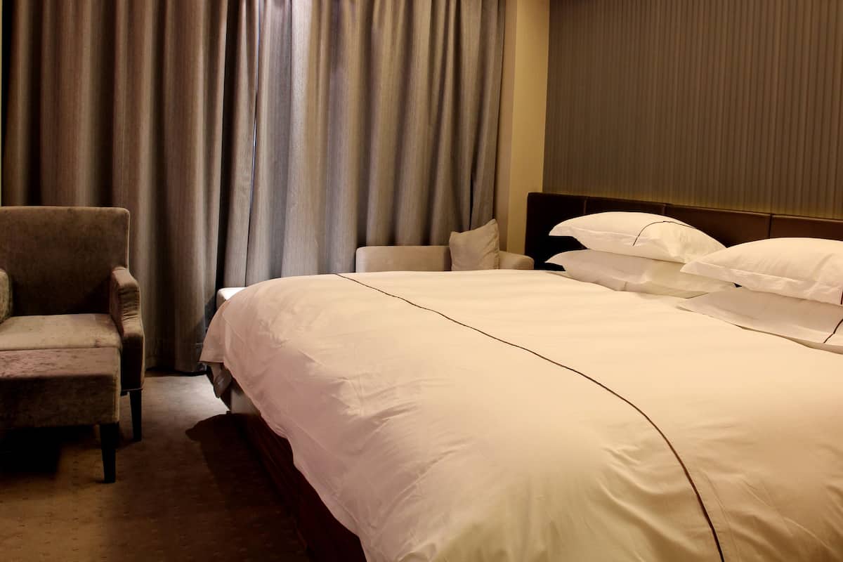 A hotel room with a large bed, a chair, and a window with curtains.