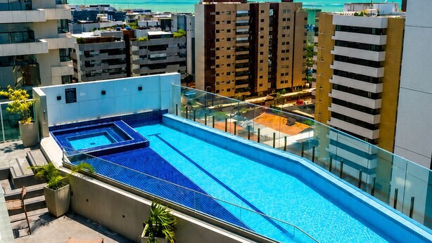 A rooftop swimming pool with a view of the ocean, surrounded by modern buildings.