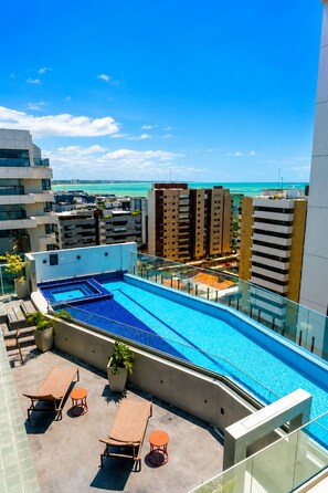 A rooftop swimming pool with a view of the ocean, surrounded by modern buildings.