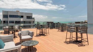 A rooftop terrace with outdoor seating, a view of the ocean, and modern buildings in the background.