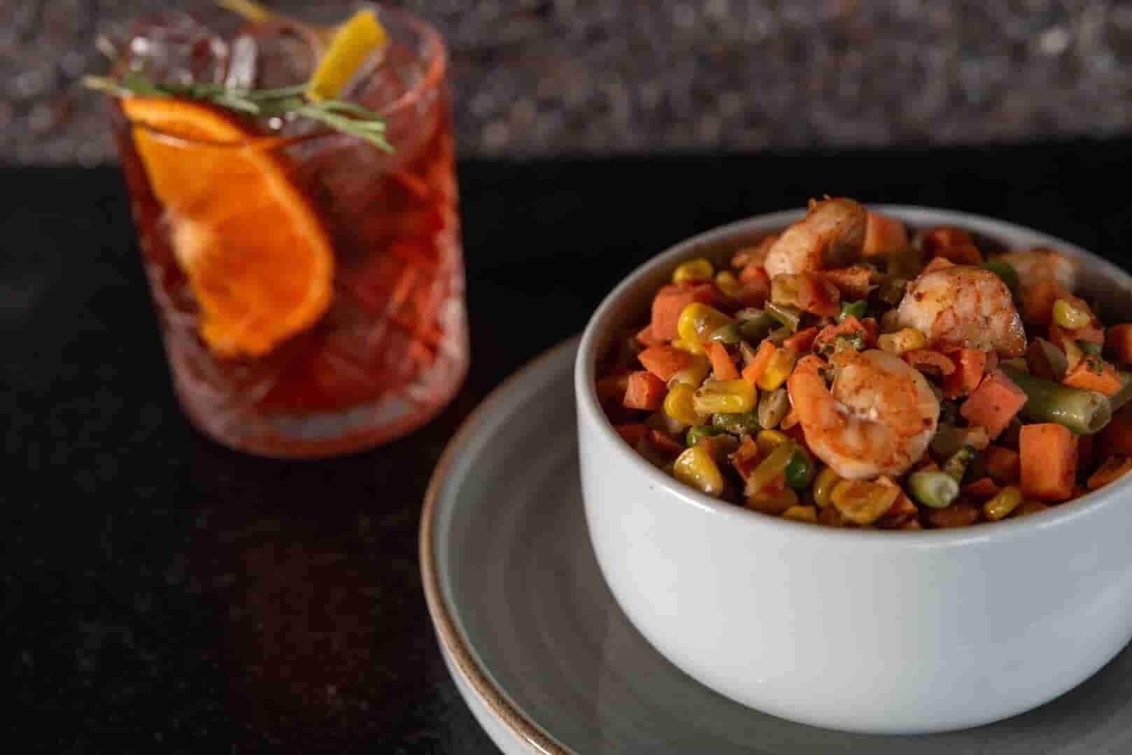 A bowl of shrimp and vegetables with a glass of iced tea with a lemon slice on the side.