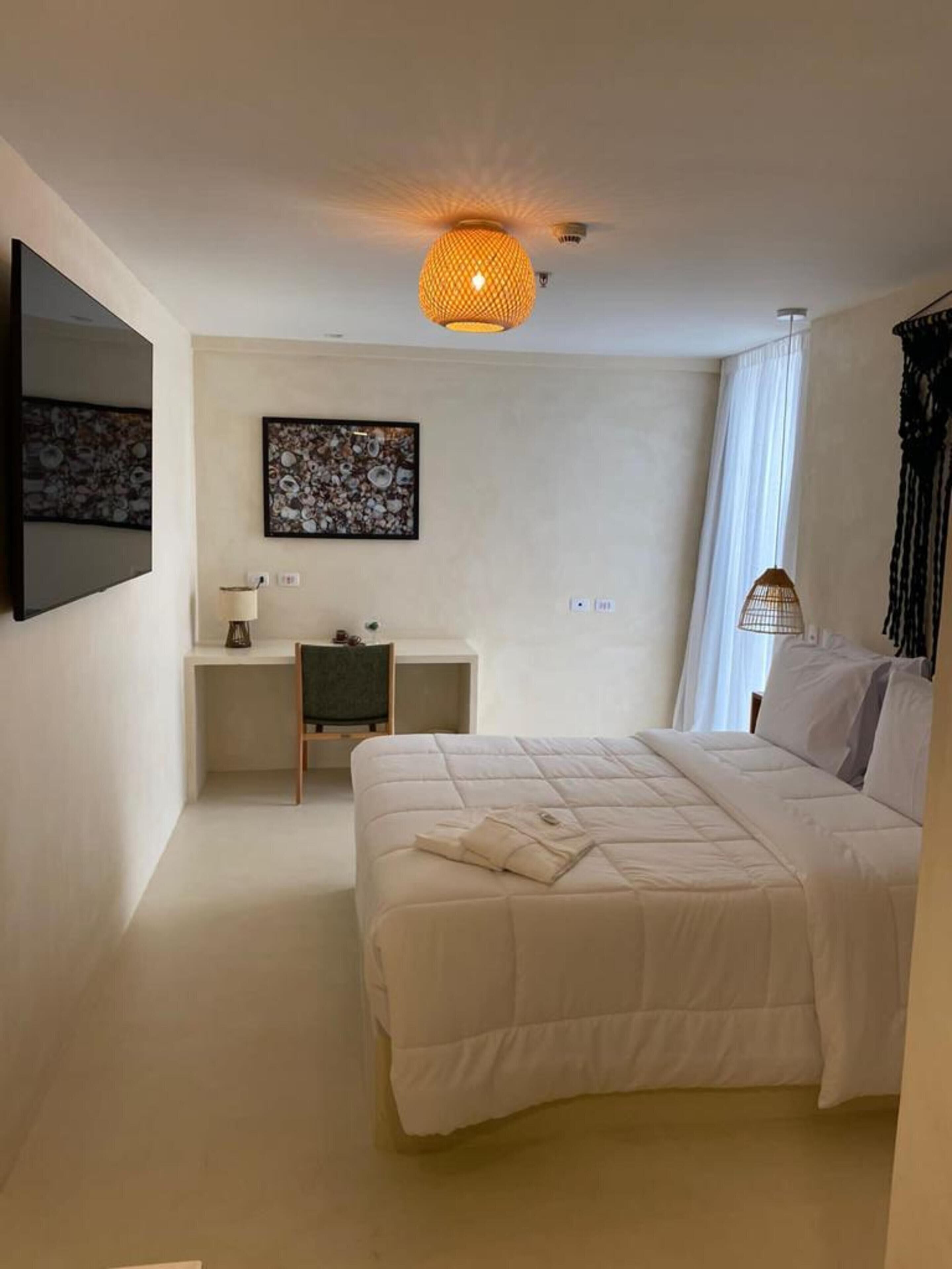 A bedroom with a bed, a desk, a chair, a lamp, and a ceiling light fixture.