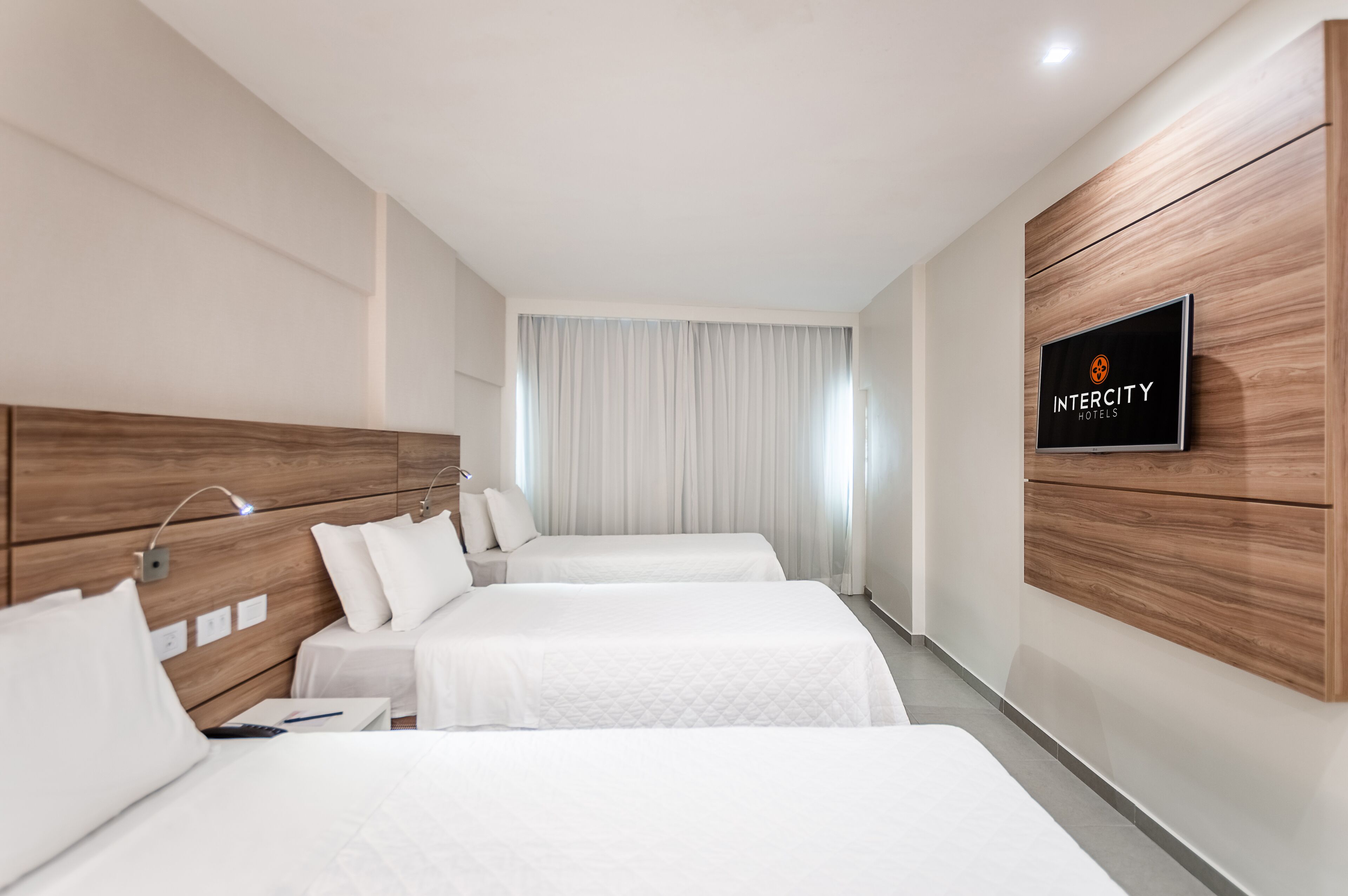 A hotel room with two beds, a TV on the wall, and a wooden headboard.