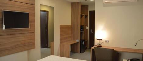 A hotel room with a bed, a desk, a chair, a TV, and an air conditioning unit.
