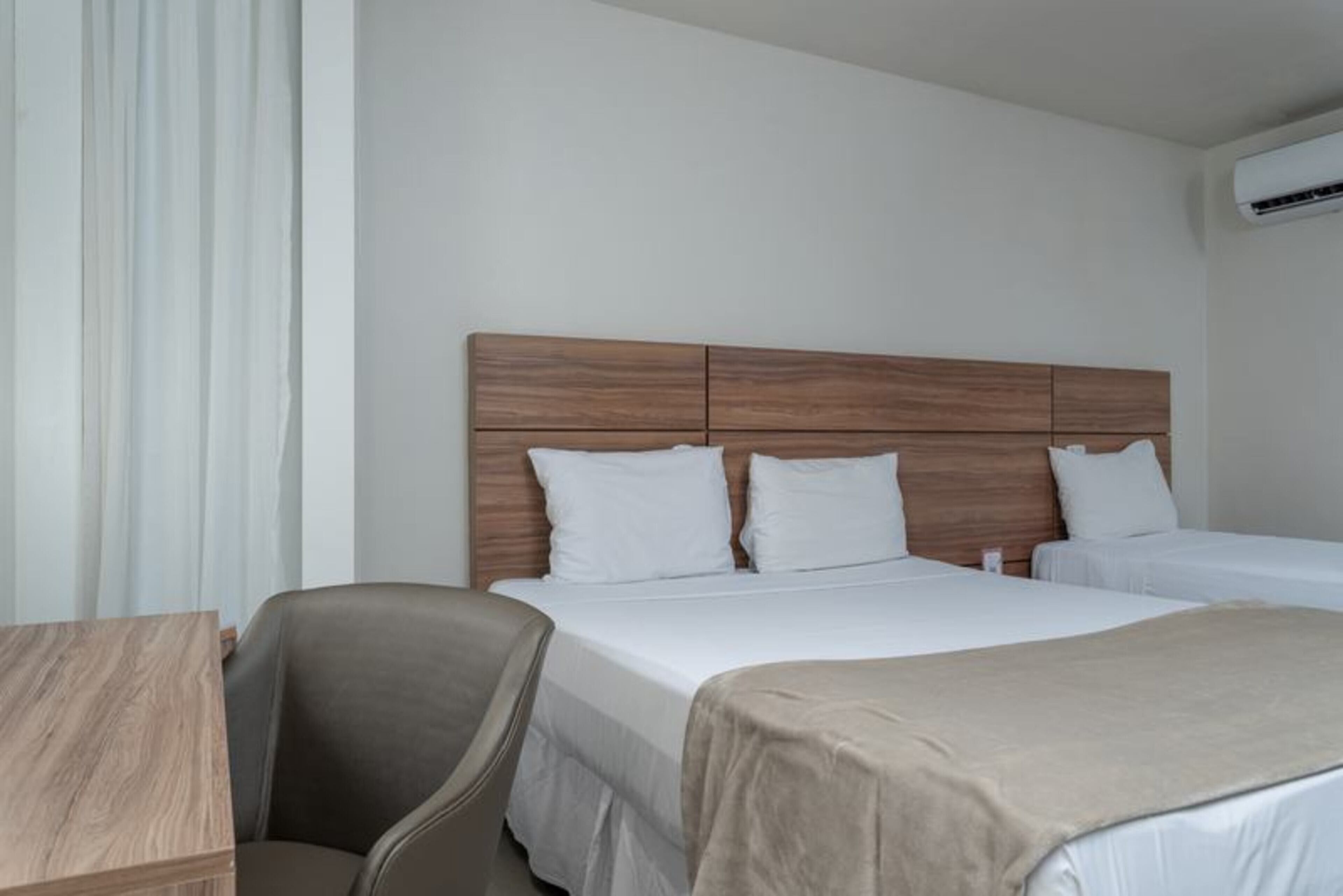 A hotel room with a wooden headboard, two beds, a desk, and a chair.