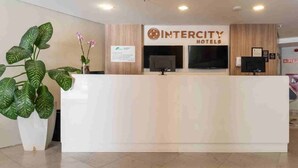 A reception desk at Intercity Hotels with a large potted plant and a sign indicating the hotel's name.