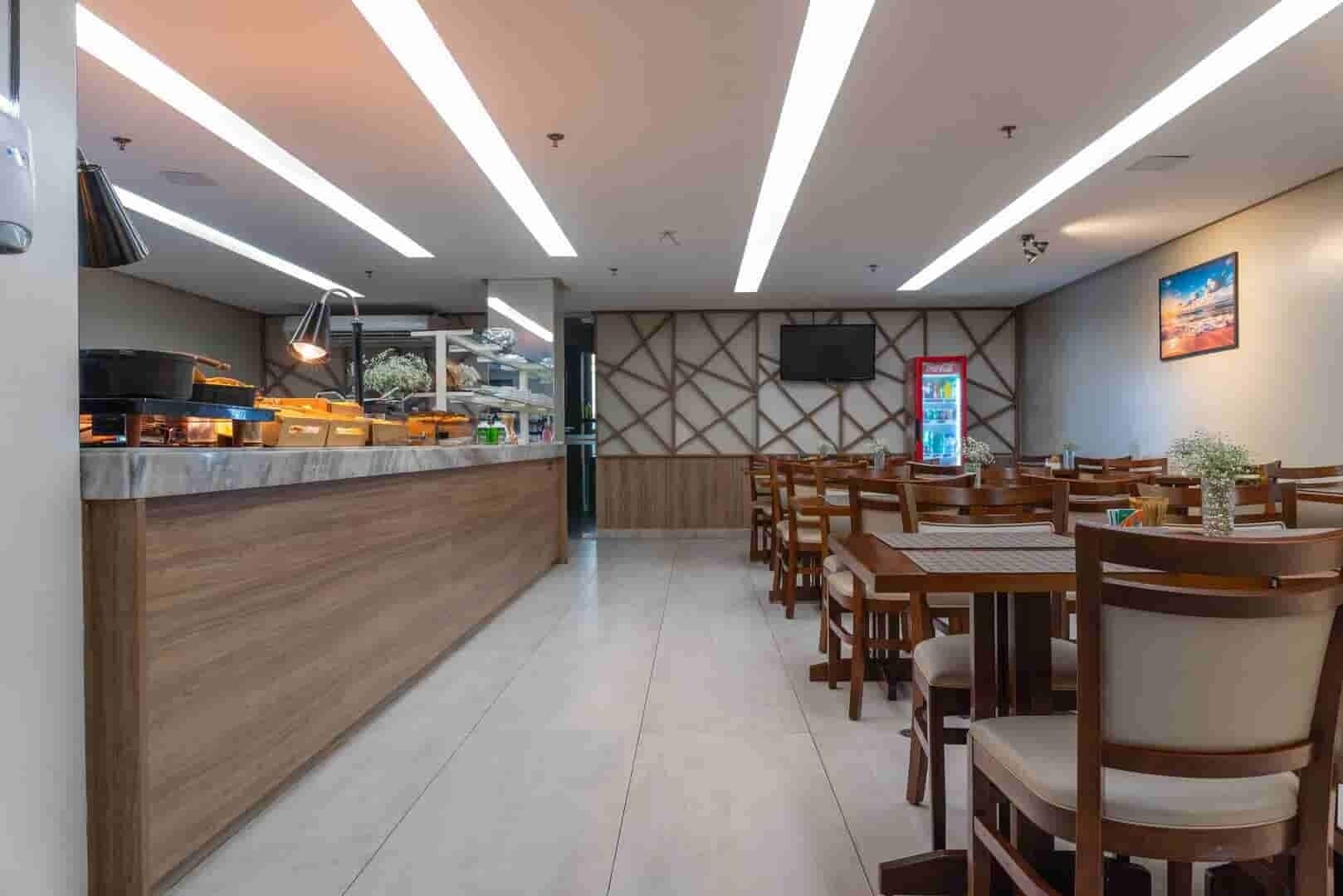 A restaurant with a long counter, wooden chairs, and a TV mounted on the wall.