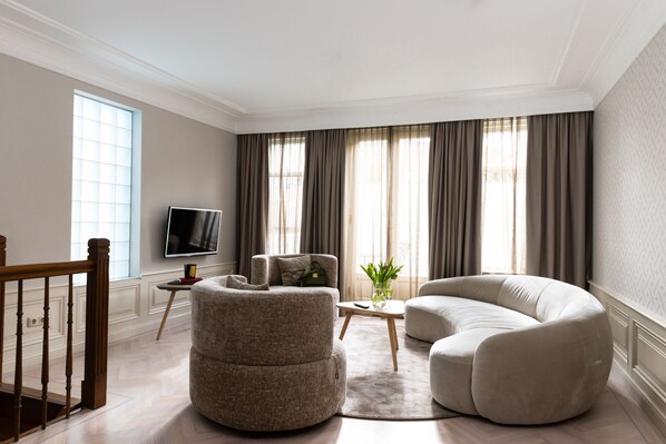 A modern living room with a wooden staircase, a flat-screen TV, and two round sofas. - Canal Suites Amsterdam (Amsterdam)