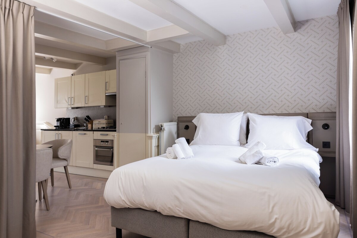 A hotel room with a bed, a desk, and a kitchenette.