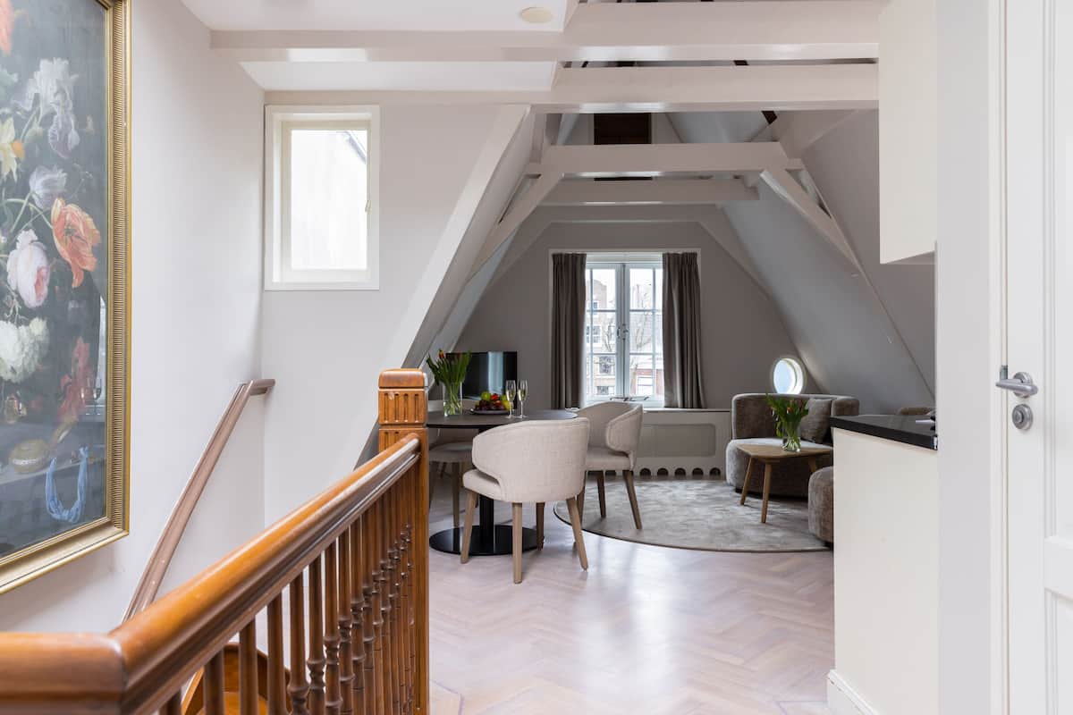 A spacious loft with a high ceiling, a dining area with a table and chairs, a seating area with a sofa, and a large painting on the wall.