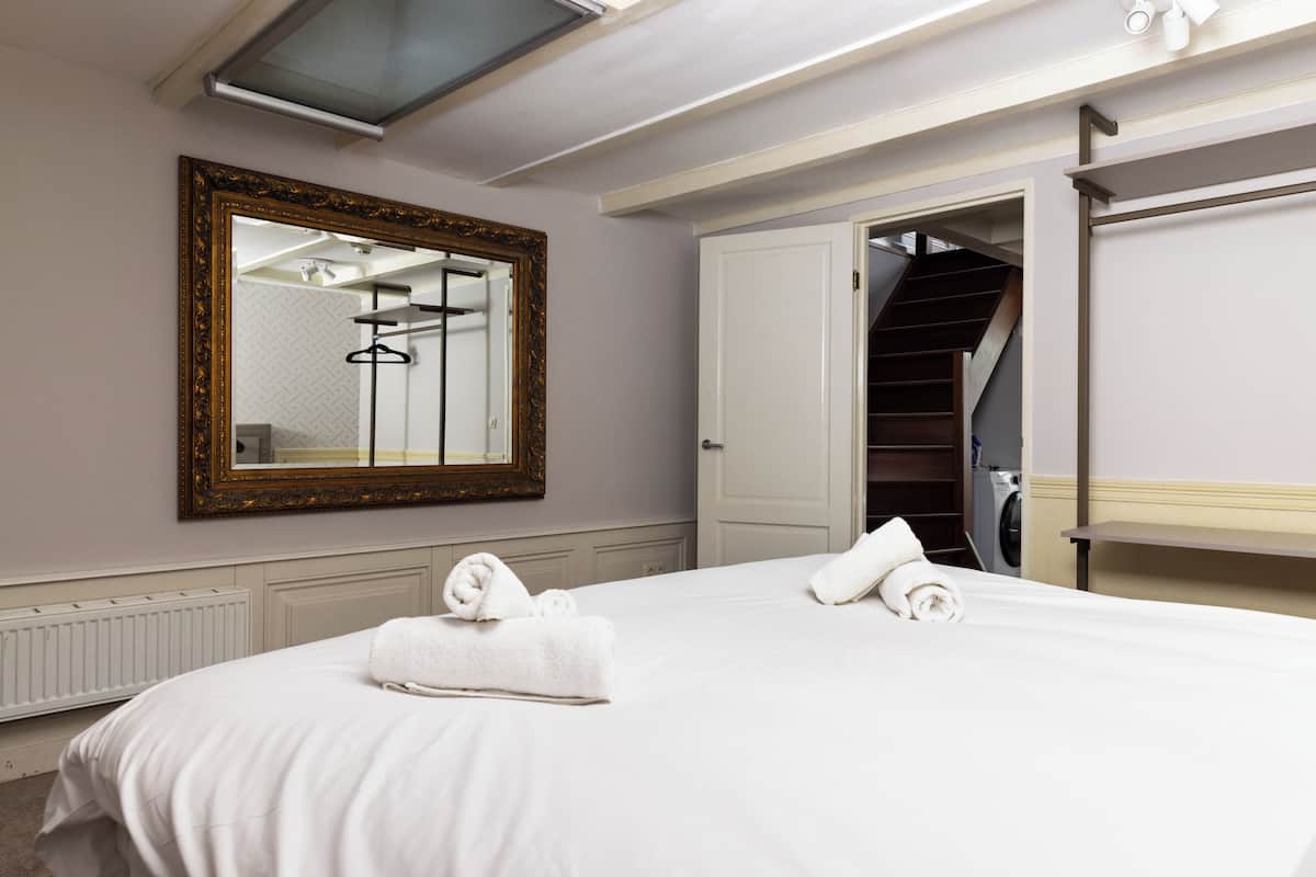 A hotel room with a large bed, a mirror, a wardrobe, and a staircase leading to another room.