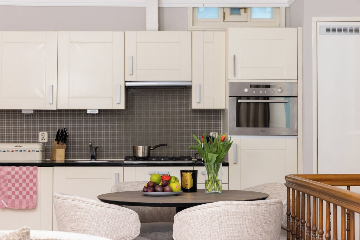 Una cocina moderna con armarios blancos, una estufa y un horno. Hay una mesa de comedor con sillas y un jarrón con flores.
