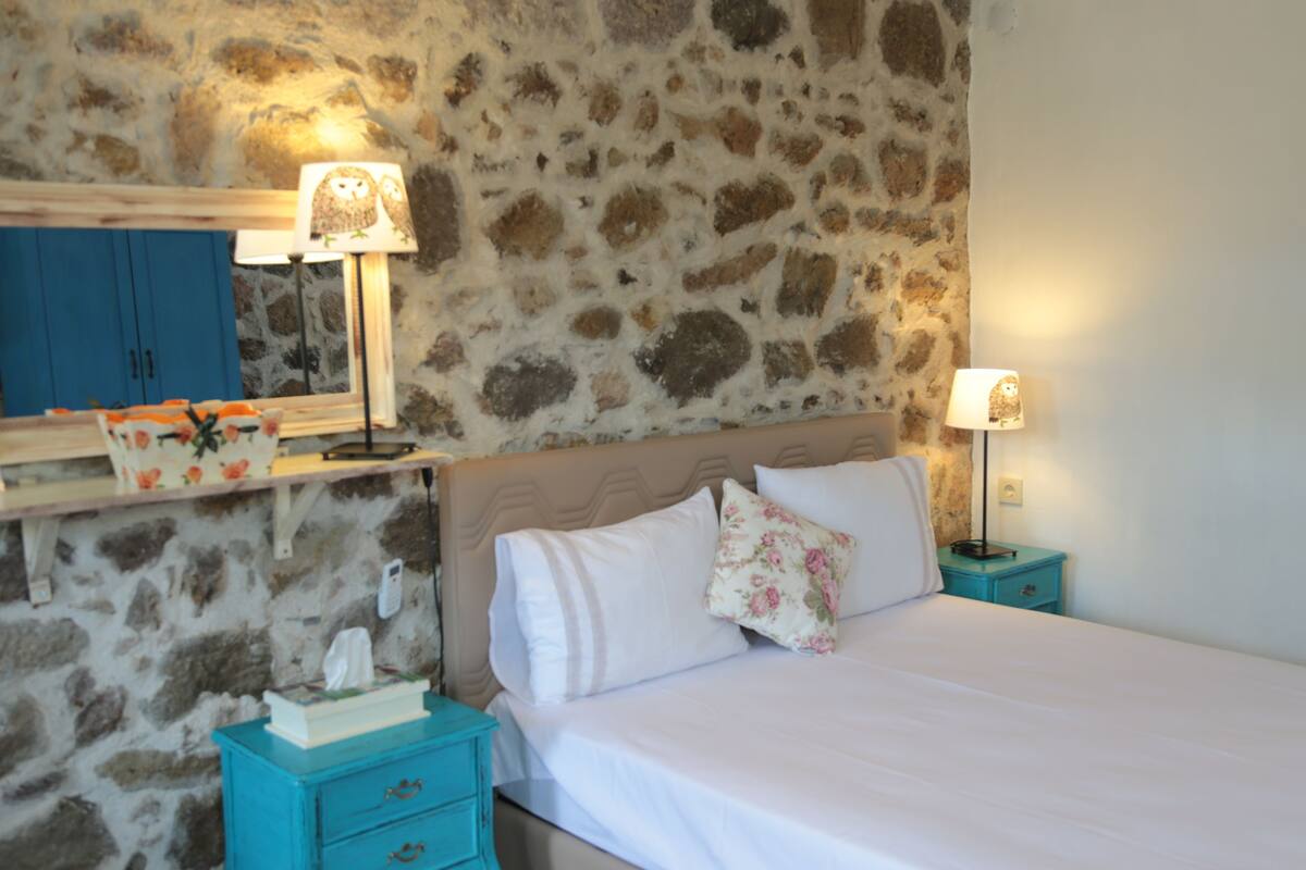 A bedroom with a stone wall, a bed with white bedding, two nightstands with lamps, and a blue cabinet with a mirror.