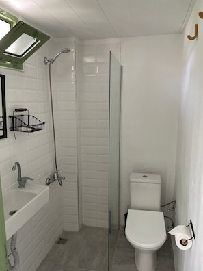 Un baño pequeño y blanco con cabina de ducha de vidrio, inodoro y lavamanos.