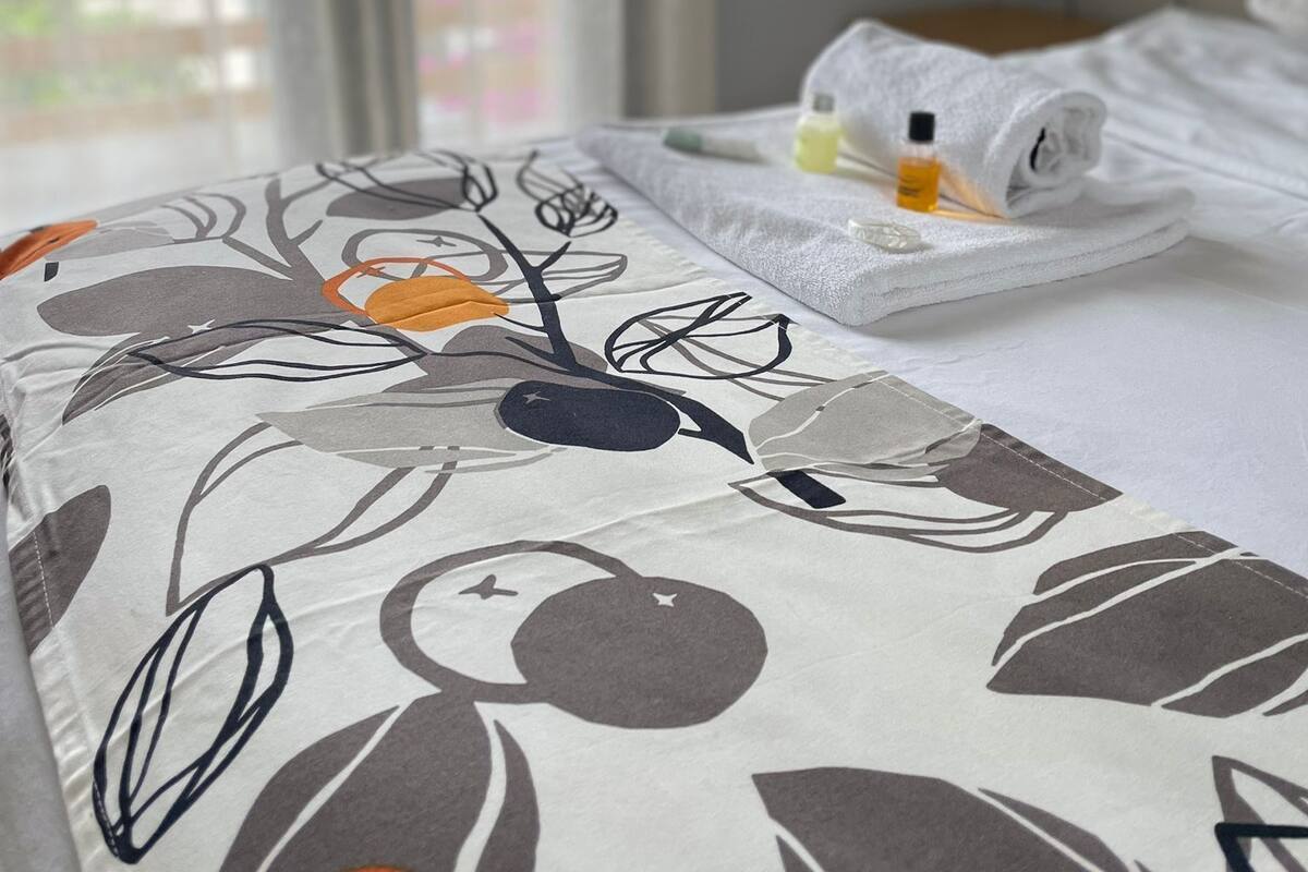 Una habitación de hotel con cama, ventana con persianas y una mesita de noche con una botella y un pañuelo.