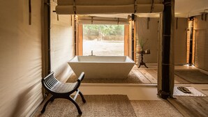 A modern bathroom with a freestanding bathtub, a bench, and a view of the outdoors. - The Beige (Angkor Thum)