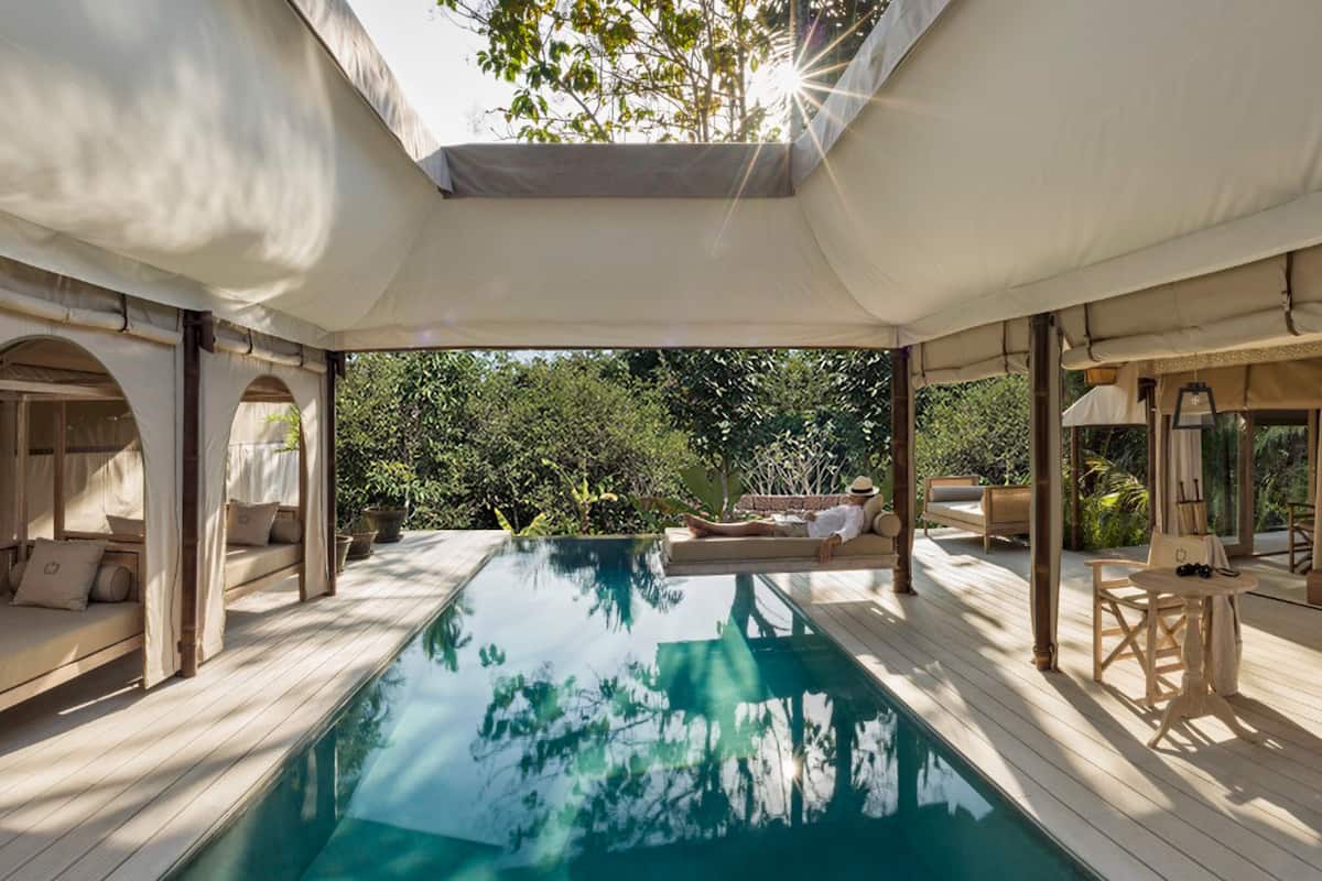 A poolside area with a clear view of the pool, wooden deck, and surrounding greenery.
