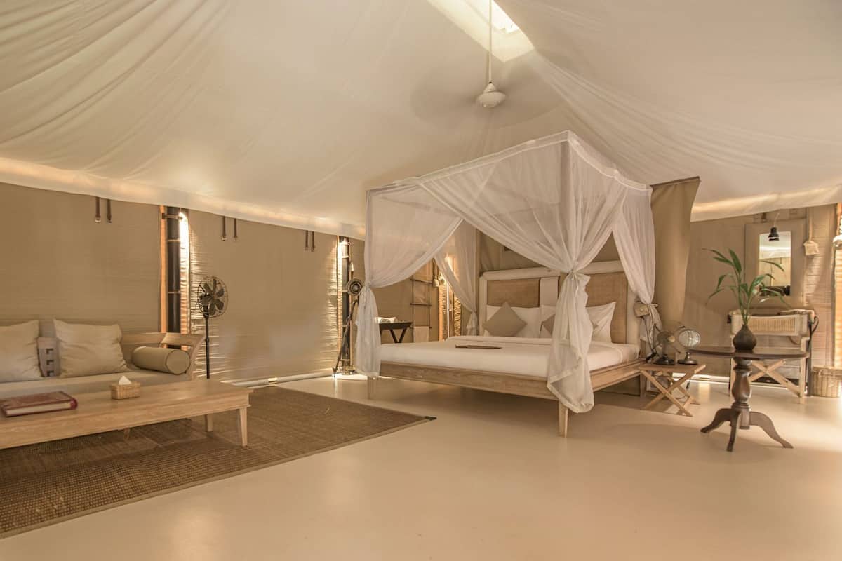 A spacious bedroom with a canopy bed, a sitting area with a sofa and a coffee table, and a bedside table with a lamp.
