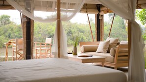 A bedroom with a bed, a wooden chair, a sofa, and a small table with a vase of plants. - The Beige (Angkor Thum)