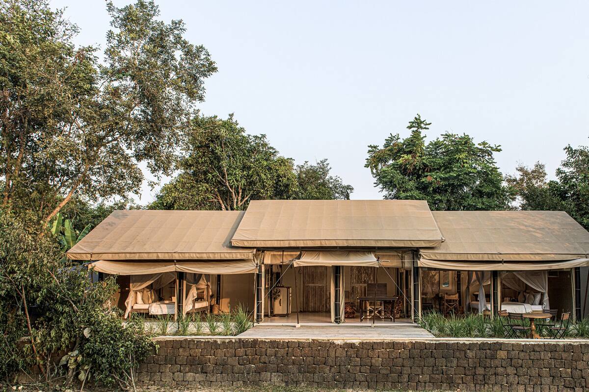 A three-room structure with a stone wall foundation, each room featuring a bed and a table.