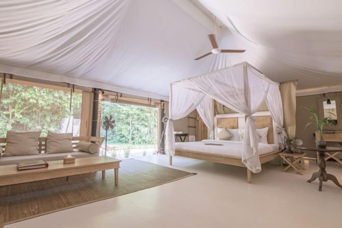 A bedroom with a canopy bed, a sofa, a small table, and a ceiling fan.