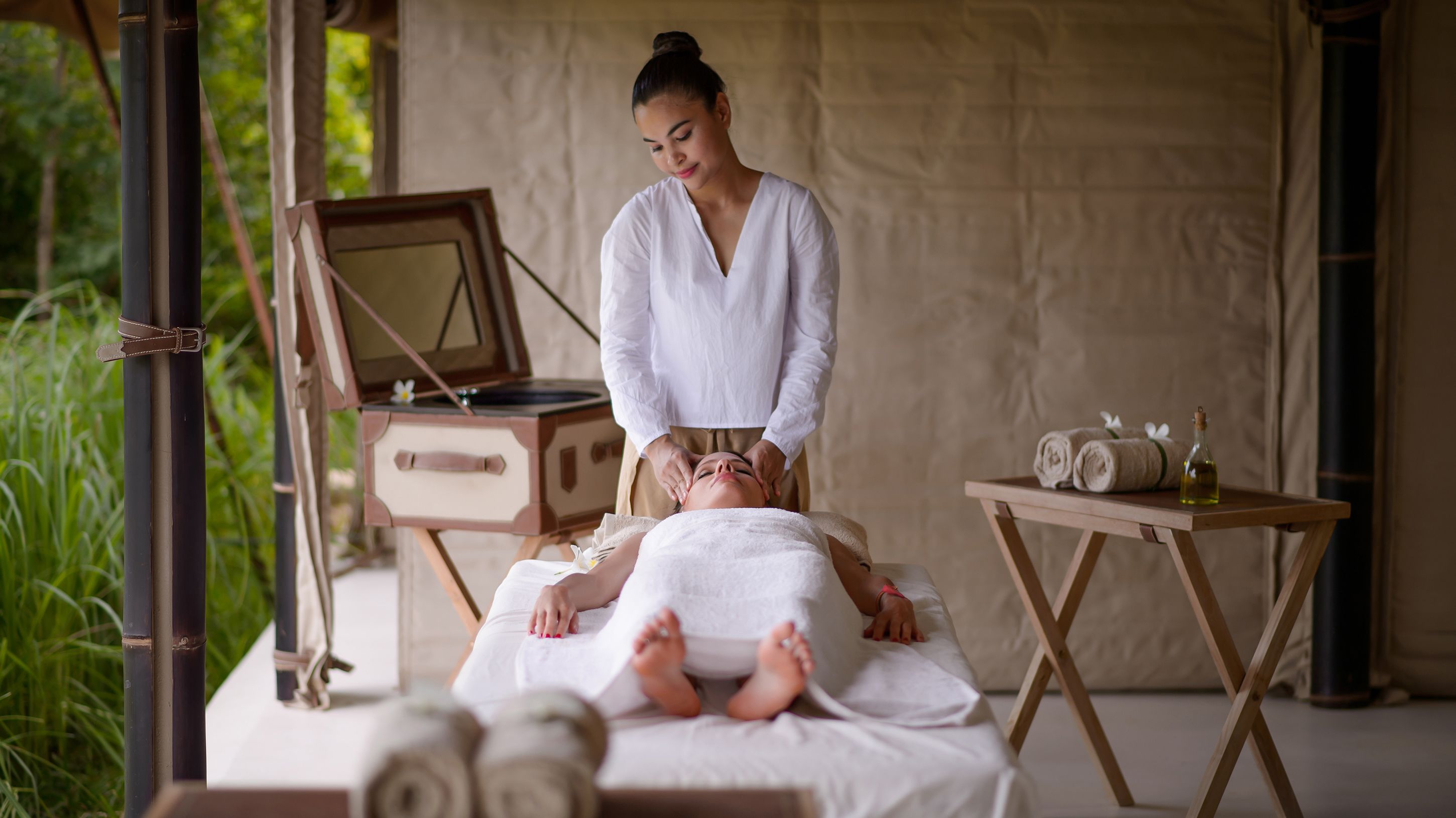 Un espace de bien-être comprenant une table de massage, un meuble en bois avec un miroir, et une petite table avec des serviettes et une bouteille.