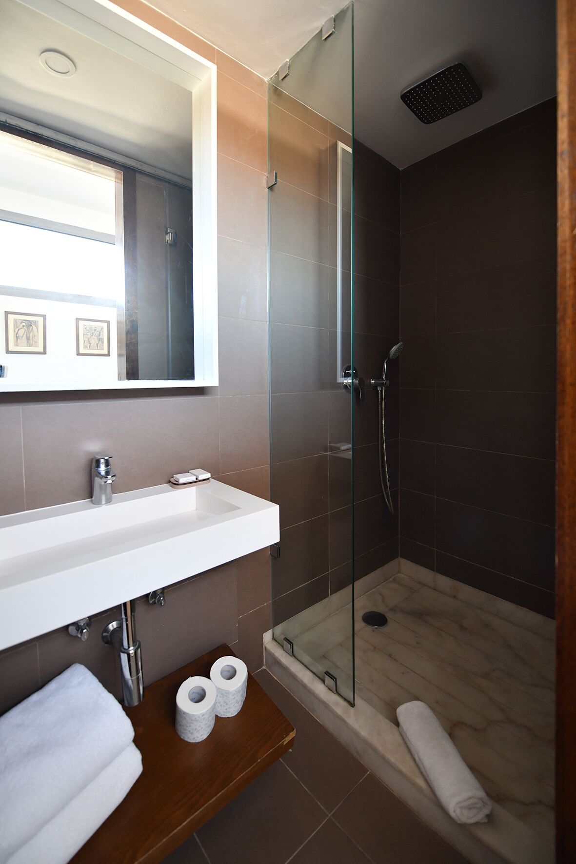 Een moderne badkamer met een douchecabine van glas, een witte wastafel en een houten wastafelmeubel.