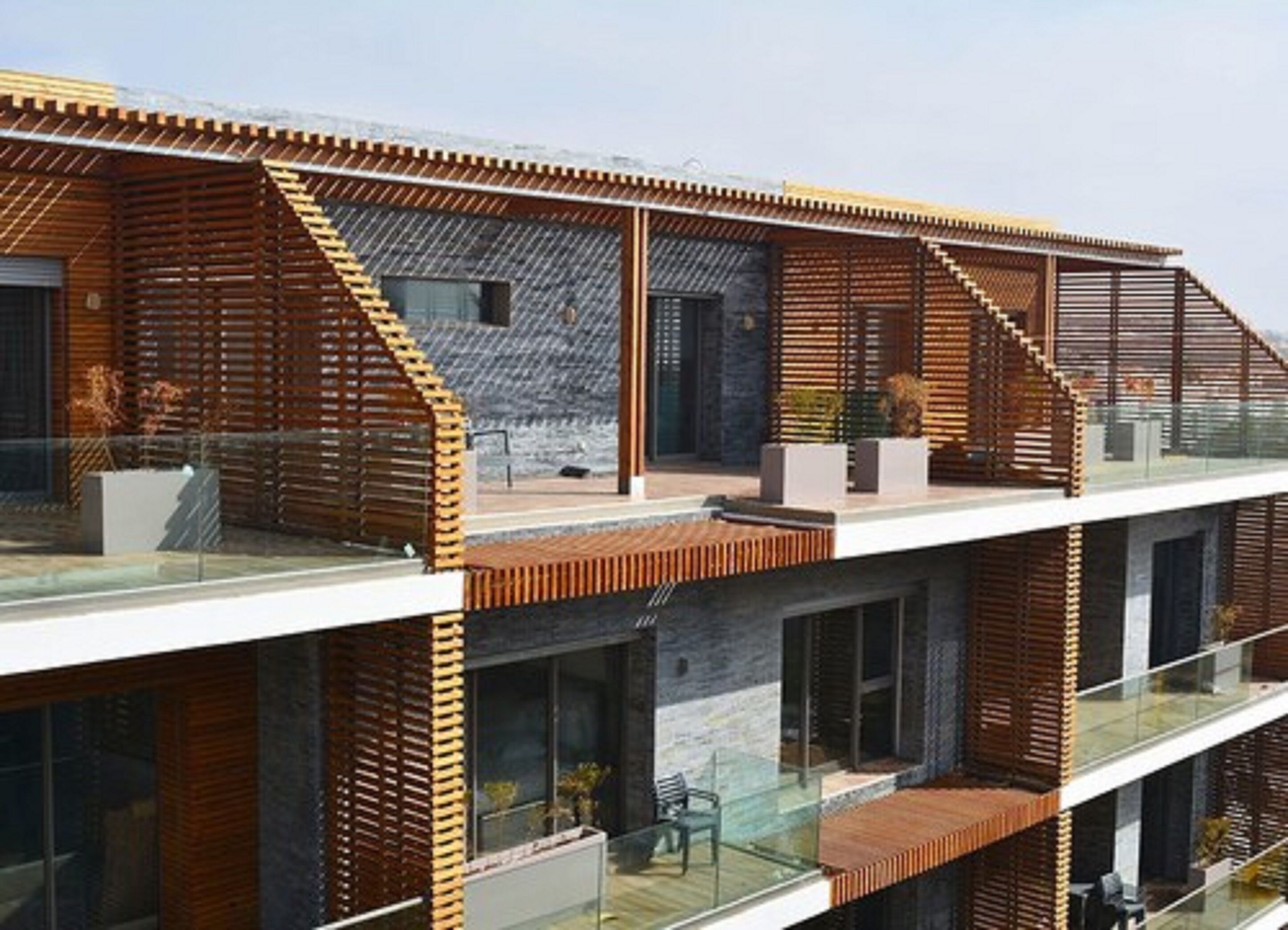 A modern multi-story building with a wooden facade, large windows, and a glass balcony.