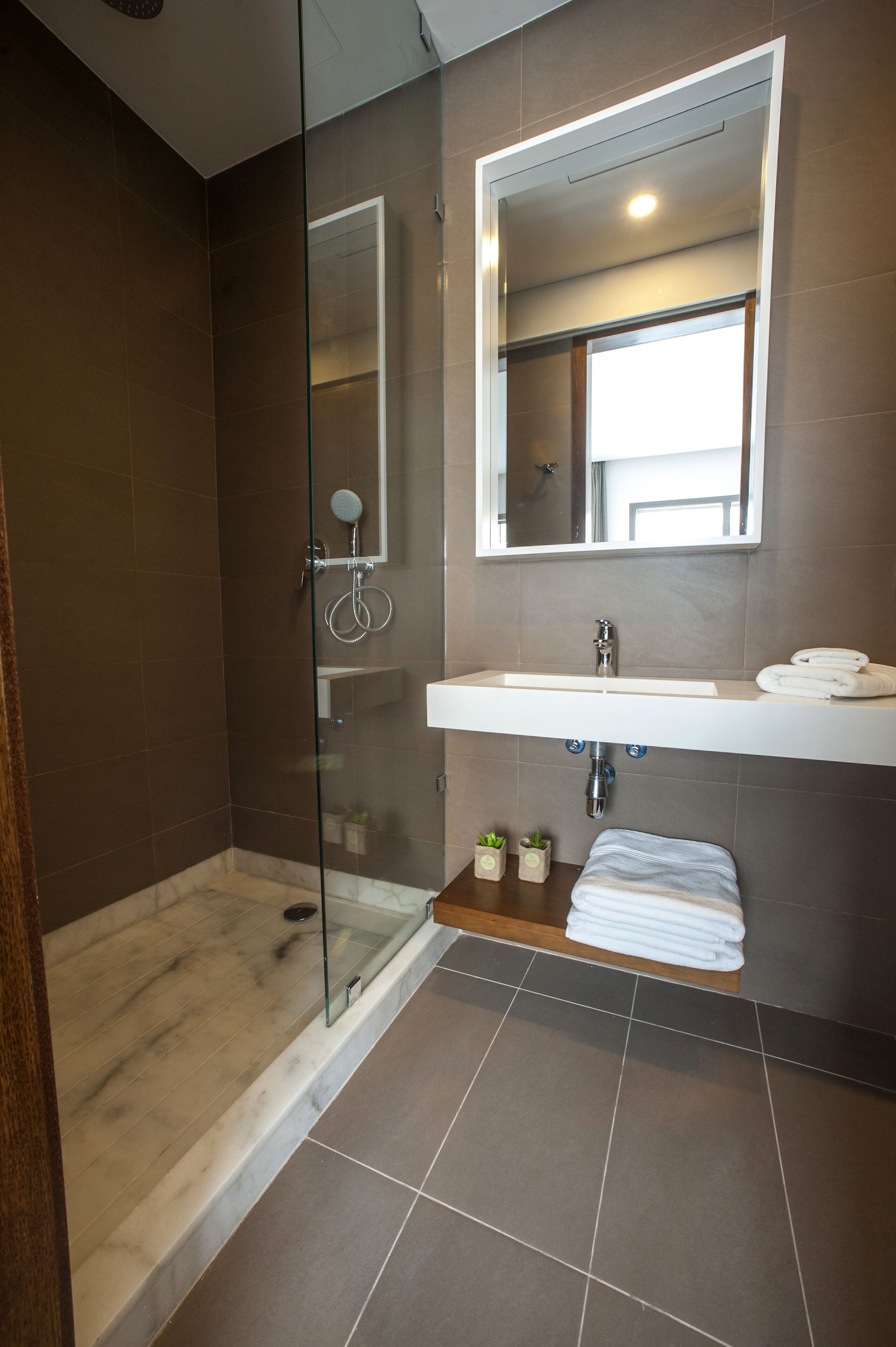 Een moderne badkamer met een douche in een glazen cabine, een witte wastafel en een spiegel erboven.