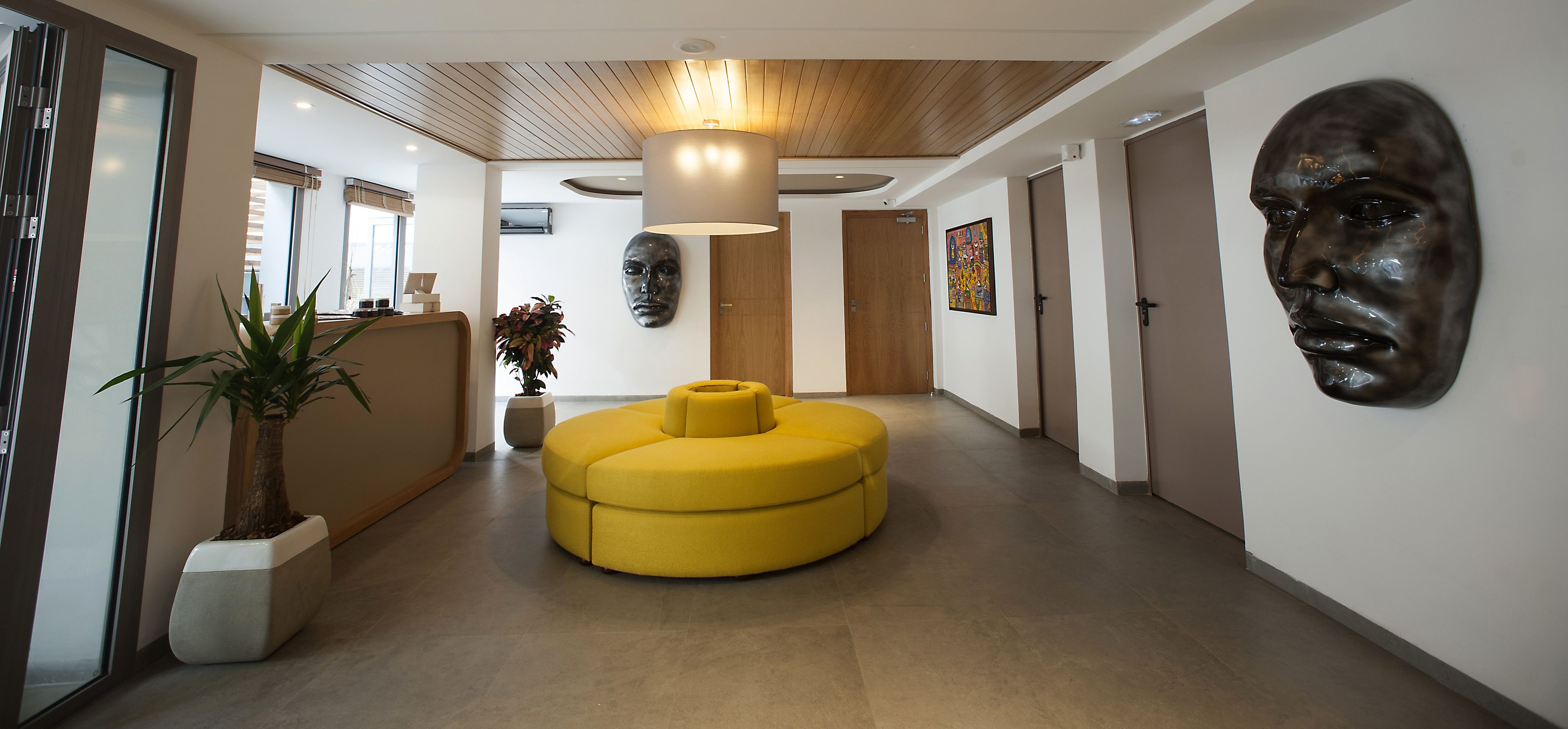 A modern hotel lobby with a central yellow seating area, a large wooden ceiling, and a wall-mounted sculpture.