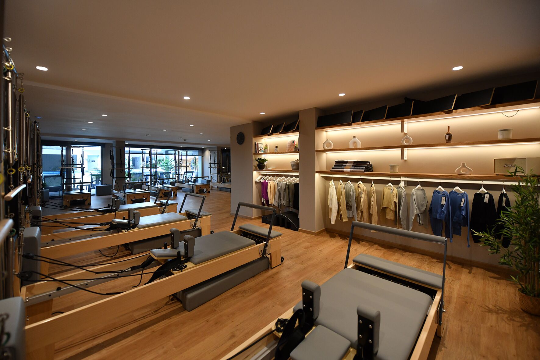 Um estúdio de fitness com equipamentos de Pilates, um cabideiro e uma grande janela com luz natural.