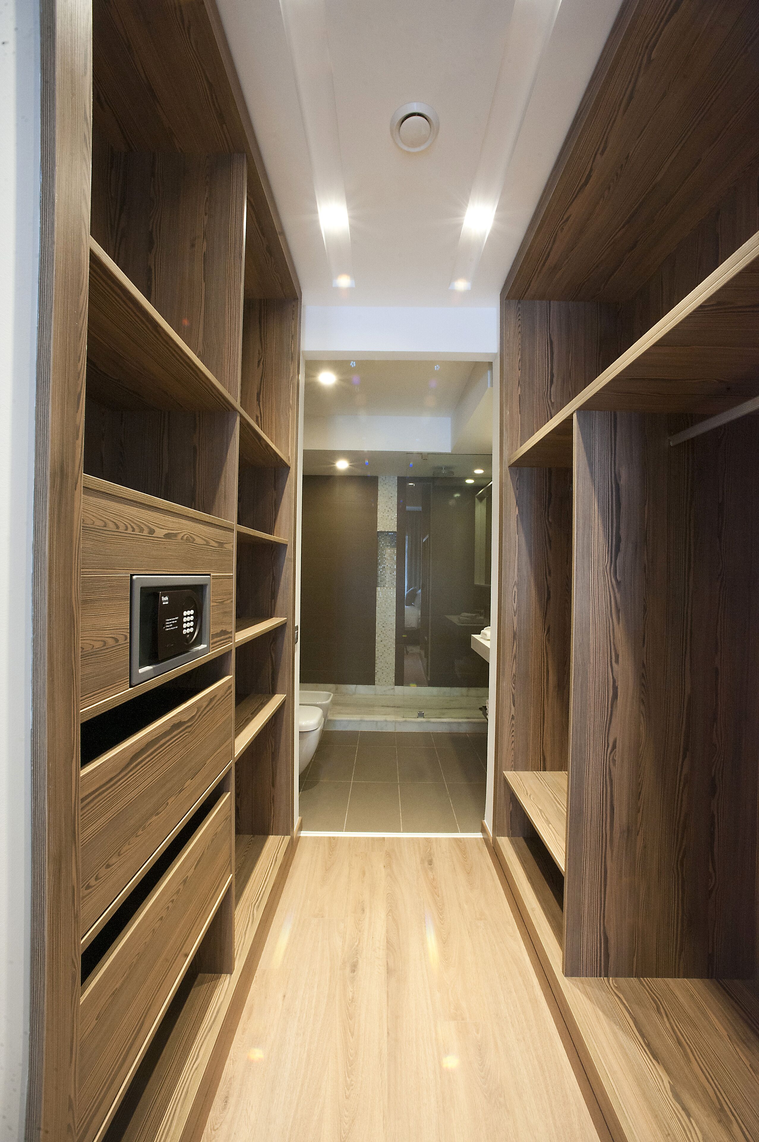 Un corridoio stretto con scaffali in legno su entrambi i lati, che conduce a un angolo bagno con doccia e servizi igienici.