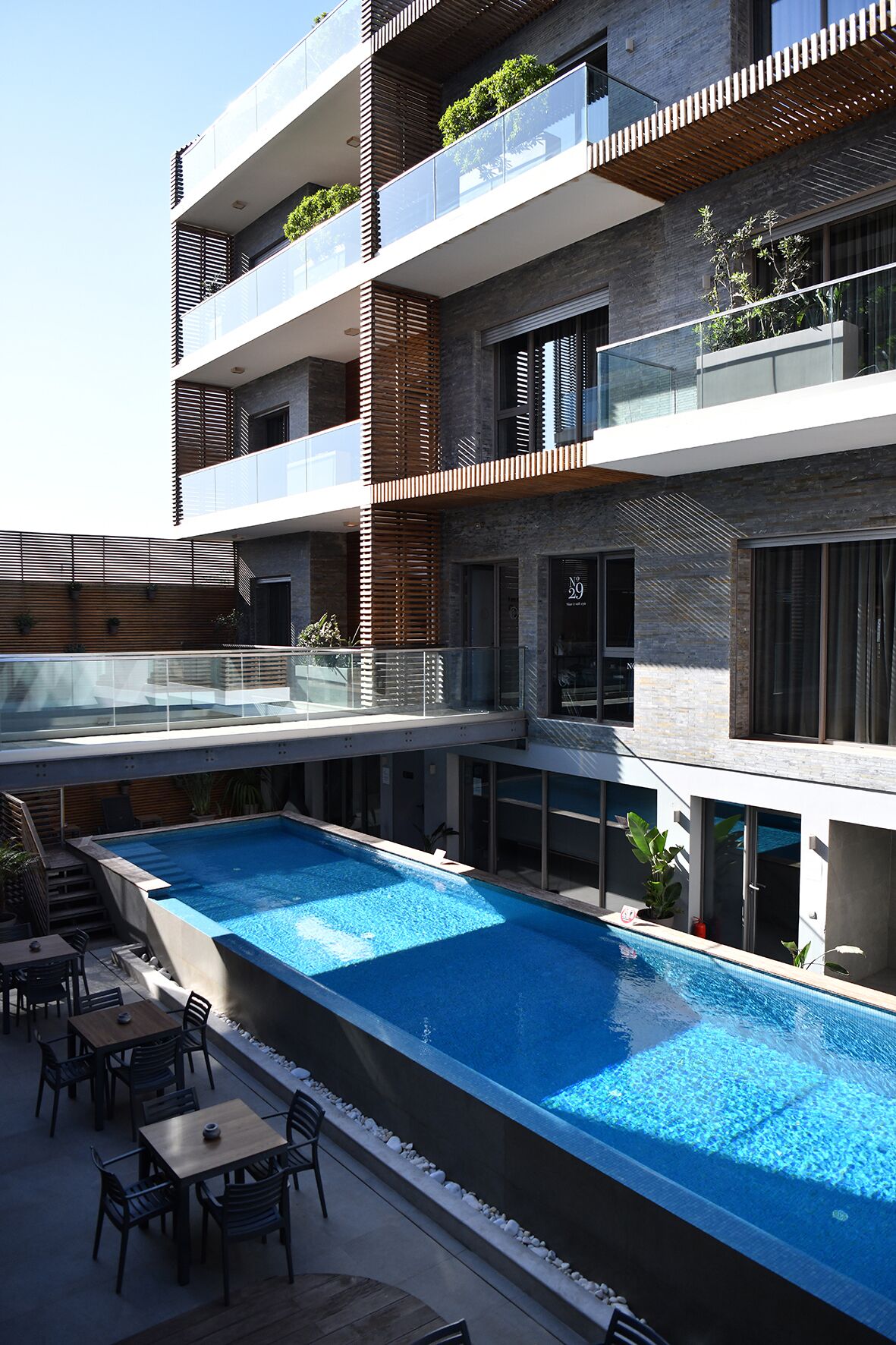 A modern building with a rooftop pool, outdoor seating, and multiple balconies with plants.