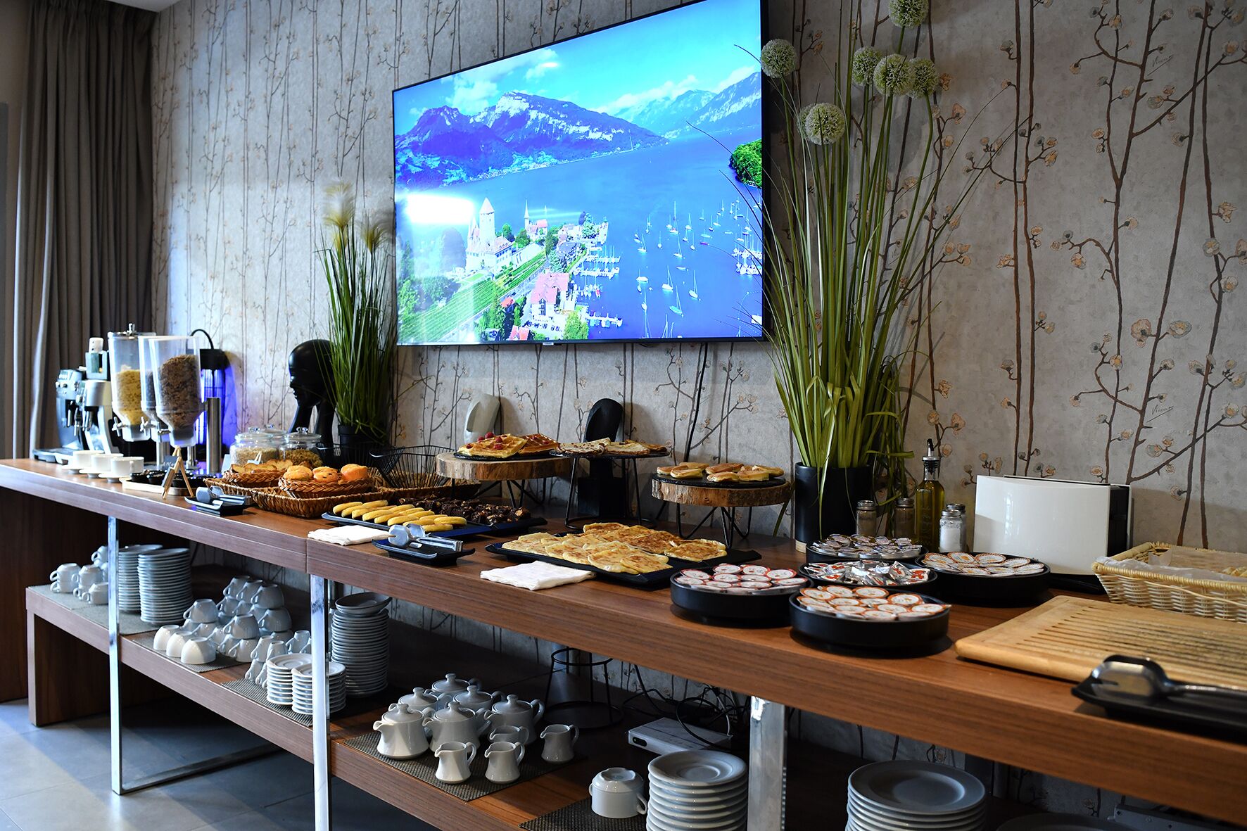 A buffet setup with various food items and a television displaying a scenic landscape.