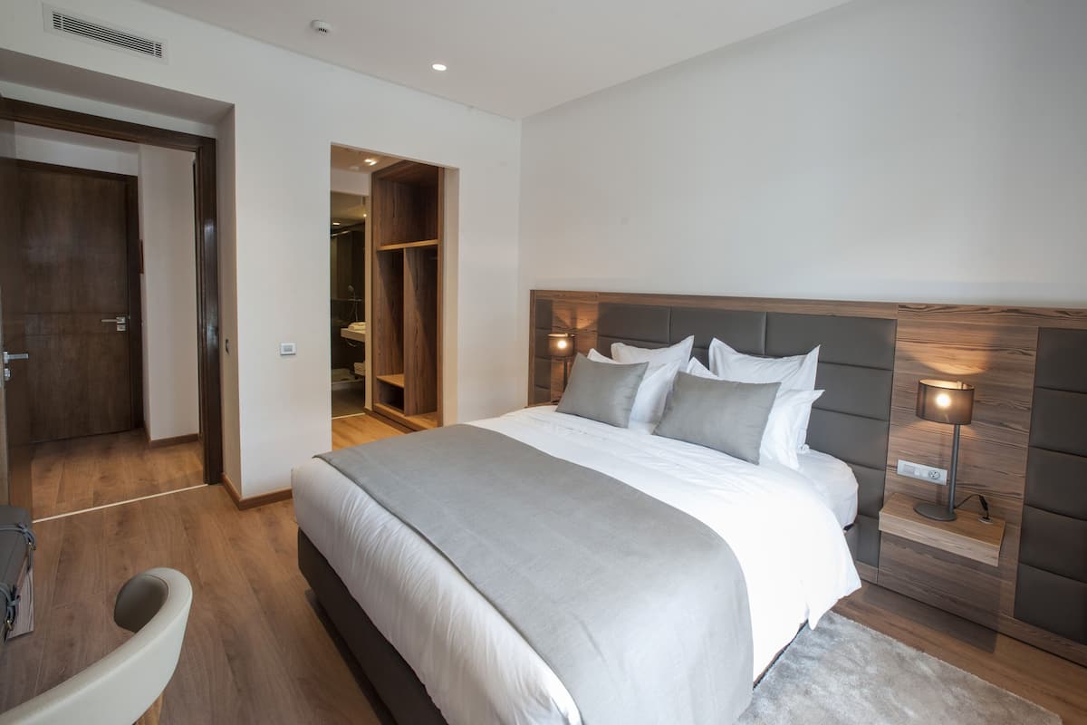 Une chambre moderne avec un grand lit, une tête de lit en bois, des lampes de chevet et un dressing.