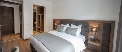 Une chambre moderne avec un grand lit, une tête de lit en bois, des lampes de chevet et un dressing.