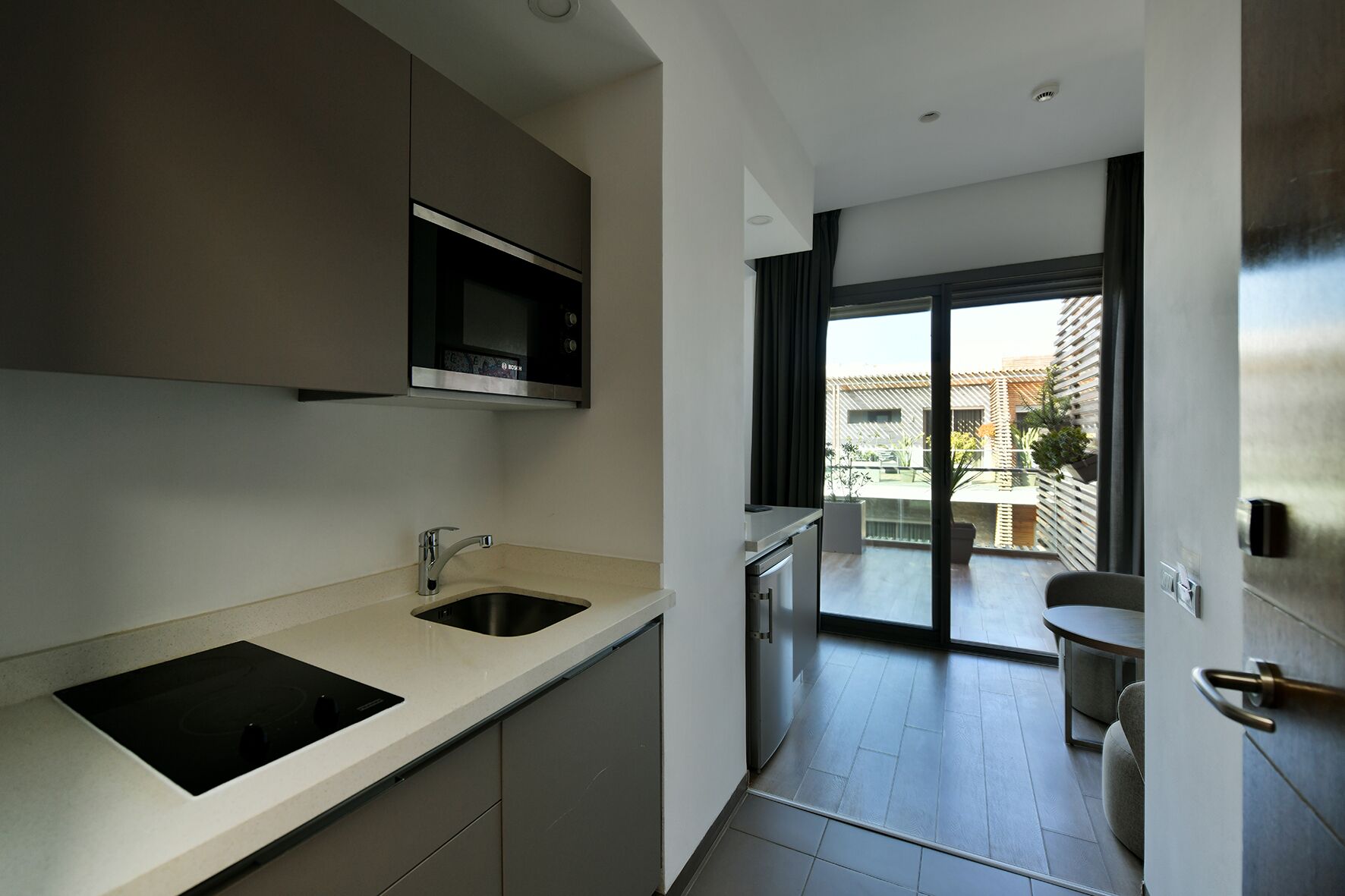 A modern kitchen with a built-in microwave, a sink, and a stove. There is a sliding glass door leading to a balcony with a view of the city.