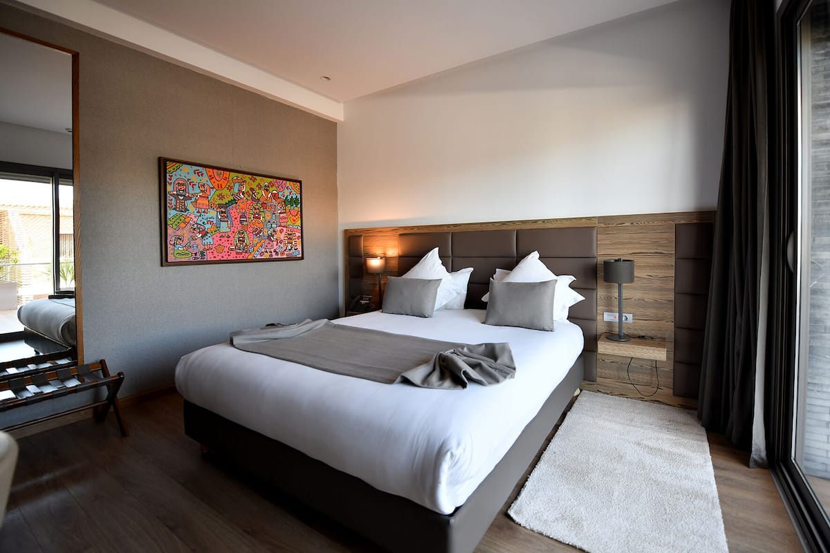 Une chambre d’hôtel moderne avec un grand lit, une table de chevet, une lampe et une œuvre d’art colorée au mur.